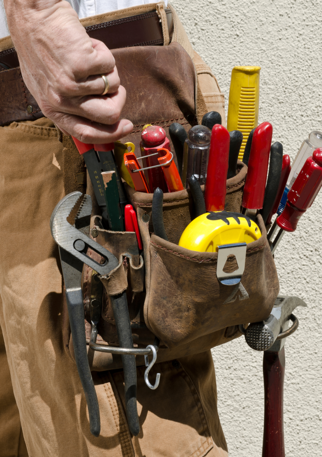 A handyman's well-worn tool belt loaded with screwdrivers, pliers, and a tape measure